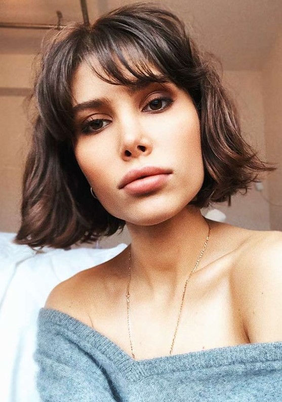 a stylish dark burnette chin-length bob with wispy bangs and messy waves is a cool idea to rock right now