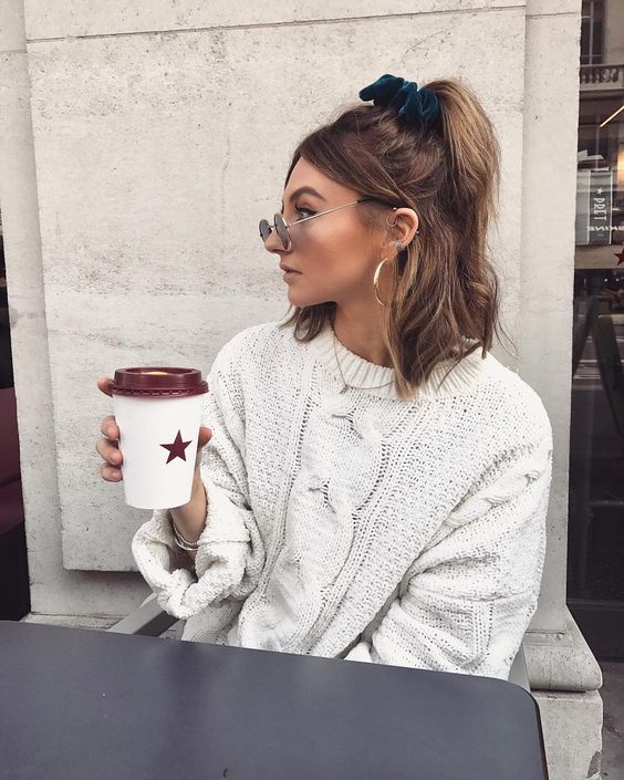 a simple and every day half updo with a ponytail and wavy hair, face-framing bangs and a green velvet scrunchie for an accent