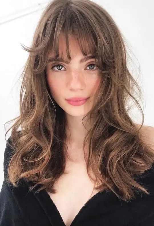 a beautiful long brunette butterfly haircut with messy waves and wispy bangs is a cool and relaxed idea to rock right now