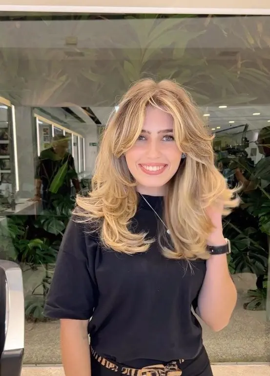 a beautiful and voluminous blonde butterfly haircut with curtain bangs, wavy ends and a lot of dimension is wow