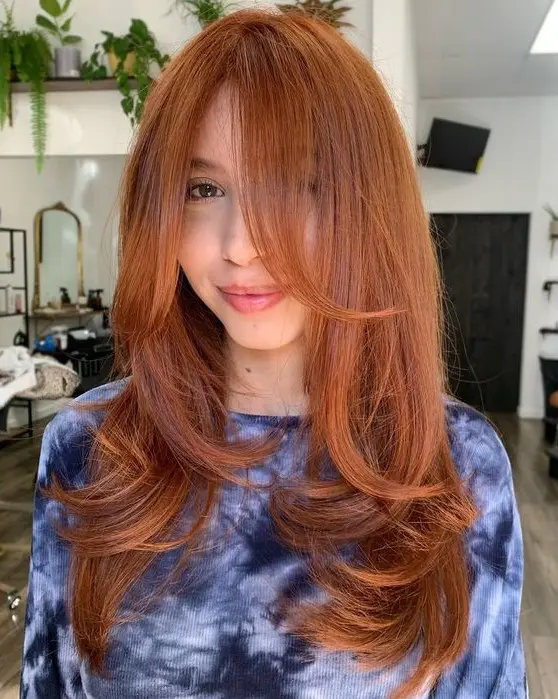 a long and beautiful ginger butterfly haircut with curled ends and bottleneck bangs is a cool and bold idea