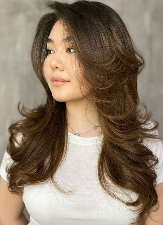 a long dark brunette butterfly haircut with caramel balayage and curled ends plus long curtain bangs