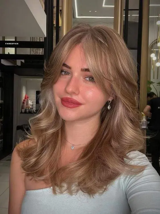 a gorgeous bronde wavy hairstyle done on a butterfly haircut, with curtain bangs, is adorable and very chic