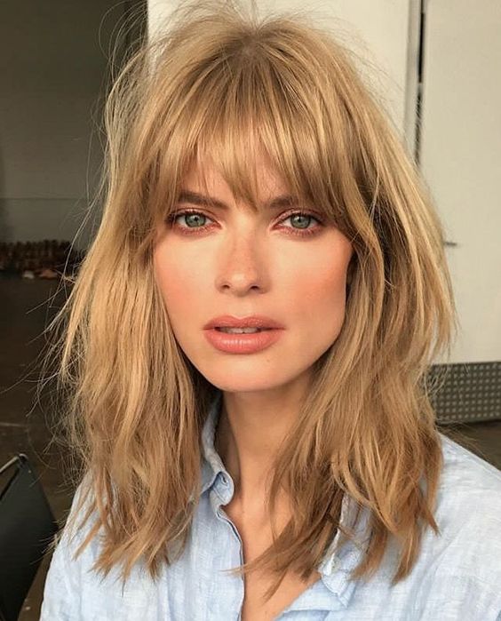 a layered honey blonde long bob with shaggy locks and with overgrown and very natural bangs is inspired by the 70s