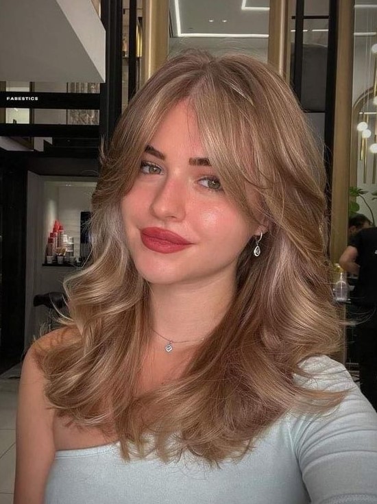 a gorgeous bronde wavy hairstyle done on a butterfly haircut, with curtain bangs, is adorable and very chic