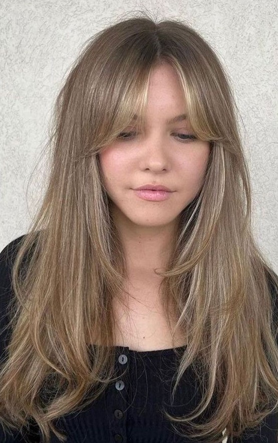 a long bronde butterfly haircut with blonde highlights and curtain bangs is a lovely idea inspired by the 70s