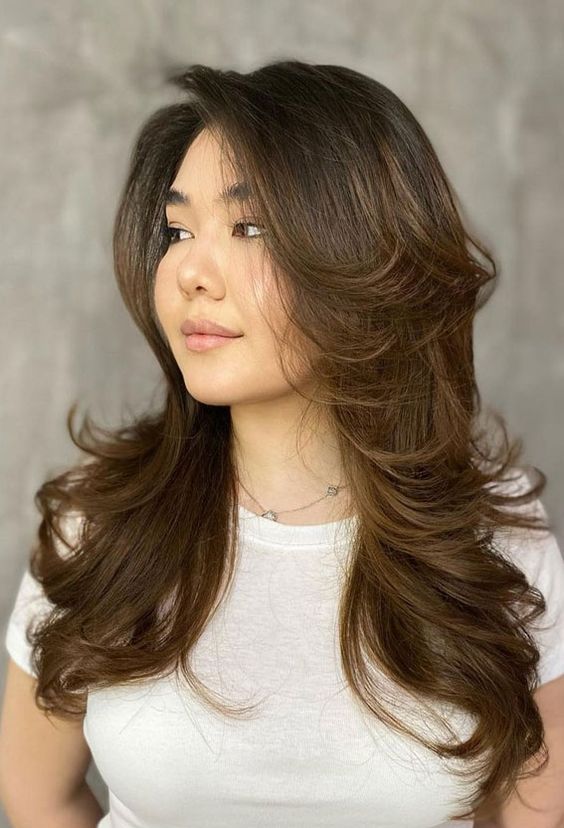 a long dark brunette butterfly haircut with caramel balayage and curled ends plus long curtain bangs