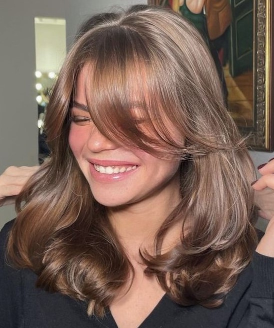 an elegant and shiny brown butterfly haircut with curtain bangs and a bit of waves to make it more dimensional