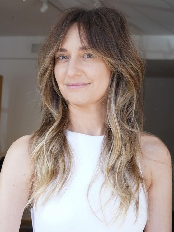 a brunette wolf cut with bottleneck bangs and waves down plus blonde balayage is a super chic idea