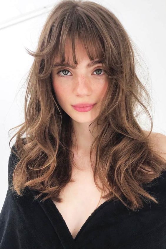 a beautiful long brunette butterfly haircut with messy waves and wispy bangs is a cool and relaxed idea to rock right now