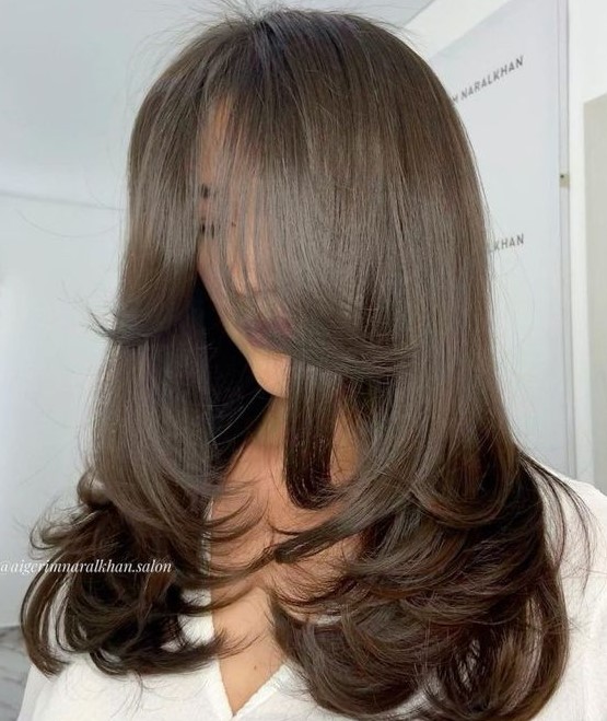 a classy butterfly haircut on dark brown hair, with layers and curved ends, with curtain bangs is pure chic and elegance