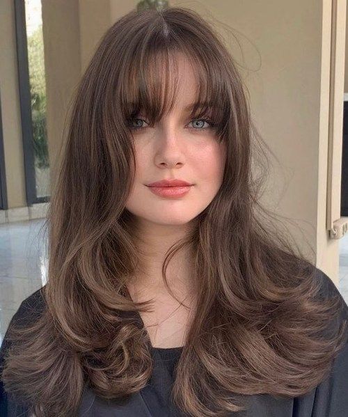 a lovely brunette butterfly haircut with waves and wispy bangs is a cool and chic idea and it shows off your locks