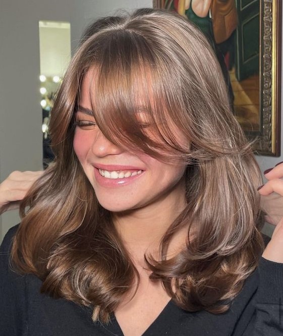 an elegant and shiny brown butterfly haircut with curtain bangs and a bit of waves to make it more dimensional