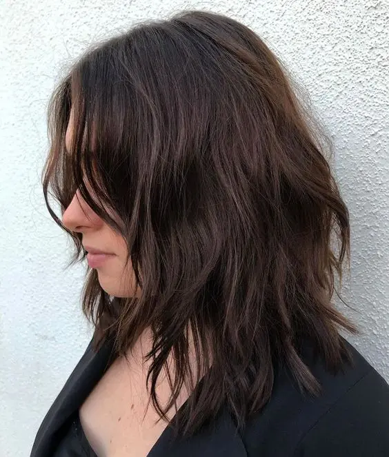 a dark brown choppy medium haircut with side bangs and messy waves shows off some texture and dimension