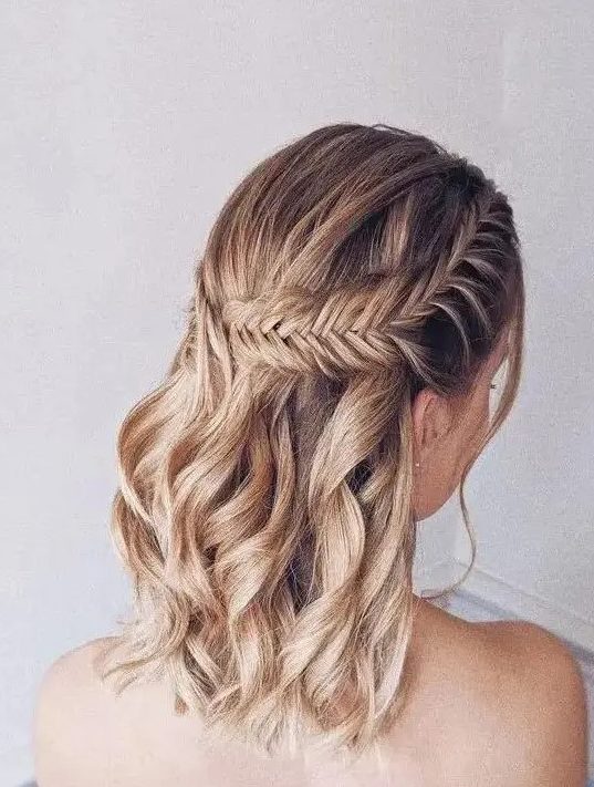 a boho half updo on medium hair, with a large fishtail braid on one side and waves down is a stylish solution