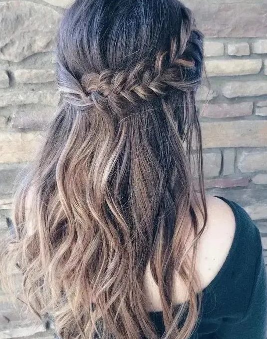 a wavy half updo with a thick fishtail braid on one side and twisted hair on the second