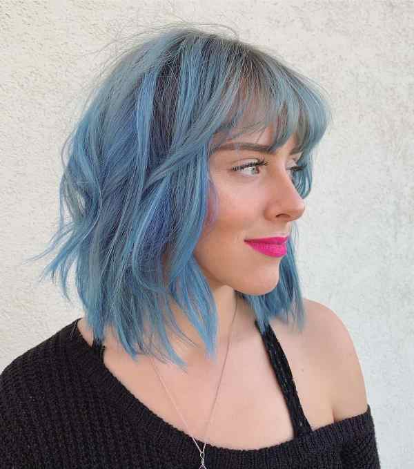 an edgy shaggy long bob with bangs done in light blue with waves that bring texture and movement to the look