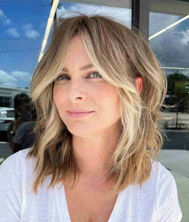 a flattering face-framing wavy lob with curtain bangs and blonde highlights and money piece is a fresh and cool idea