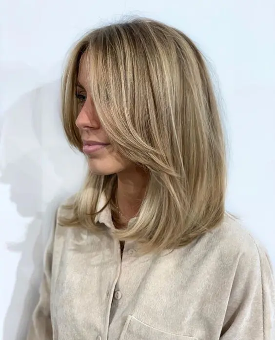 a medium-length blonde hairstyle with long curtain bangs and blonde balayage is a lovely and chic idea