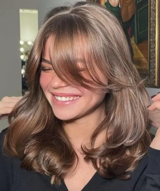 an elegant and shiny brown butterfly haircut with curtain bangs and a bit of waves to make it more dimensional