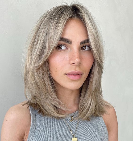 cold blonde medium length hair with a darker root and curtain bangs is a stylish and chic idea