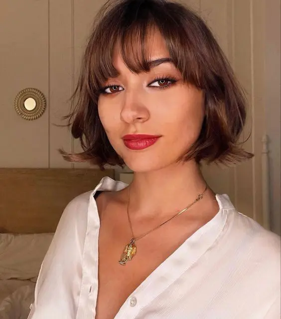 a beautiful brunette chin-length bob with wispy bangs and waves is a stylish and eye-catching idea